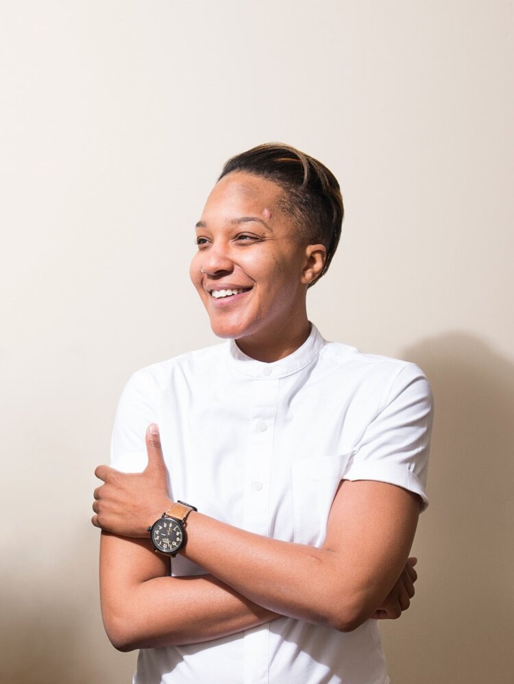 Woman in white t-shirt with arms crossed, smiling and looking to her right.