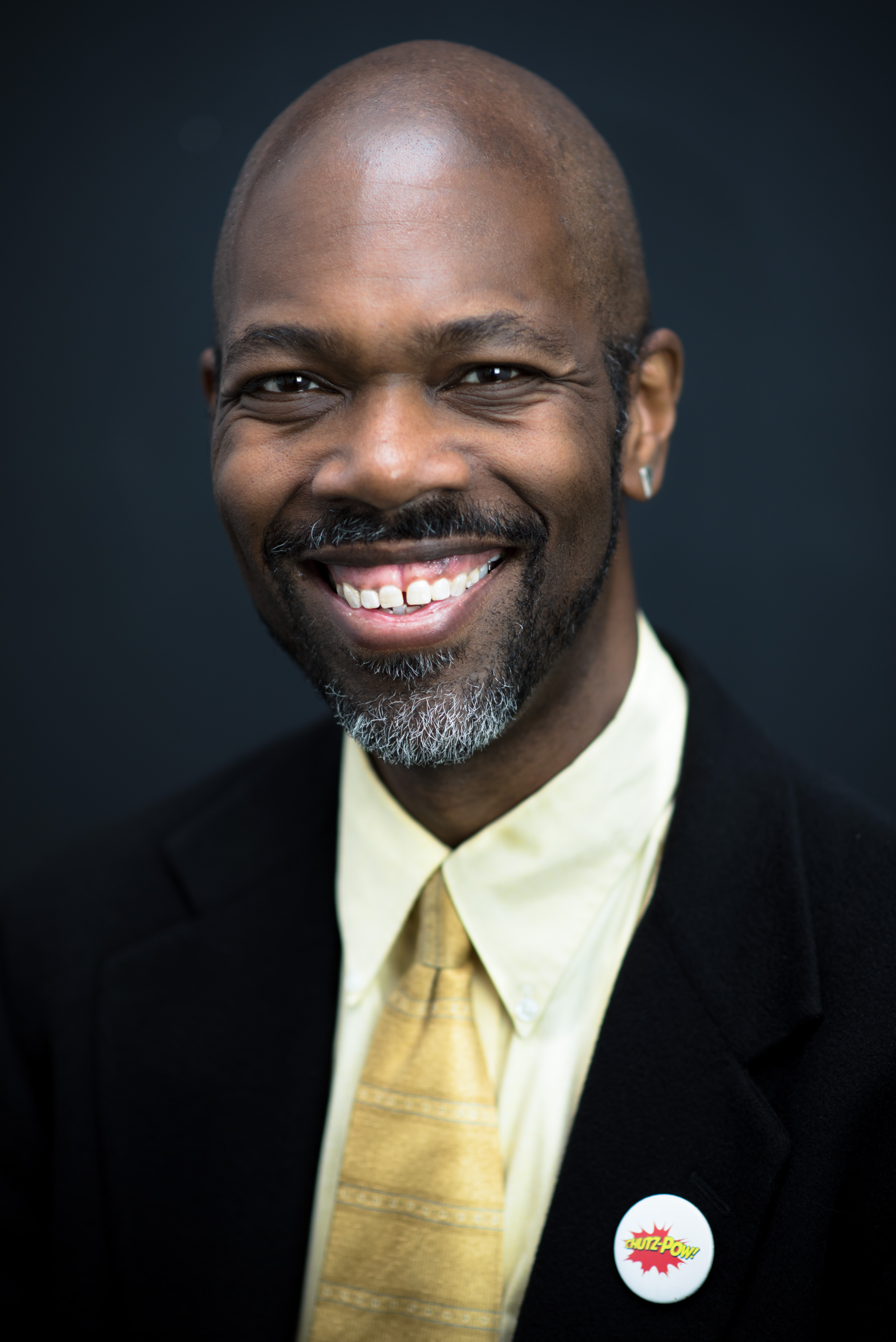 A Black man with slat and pepper beard dressed in a suit smiles widely for the camera.