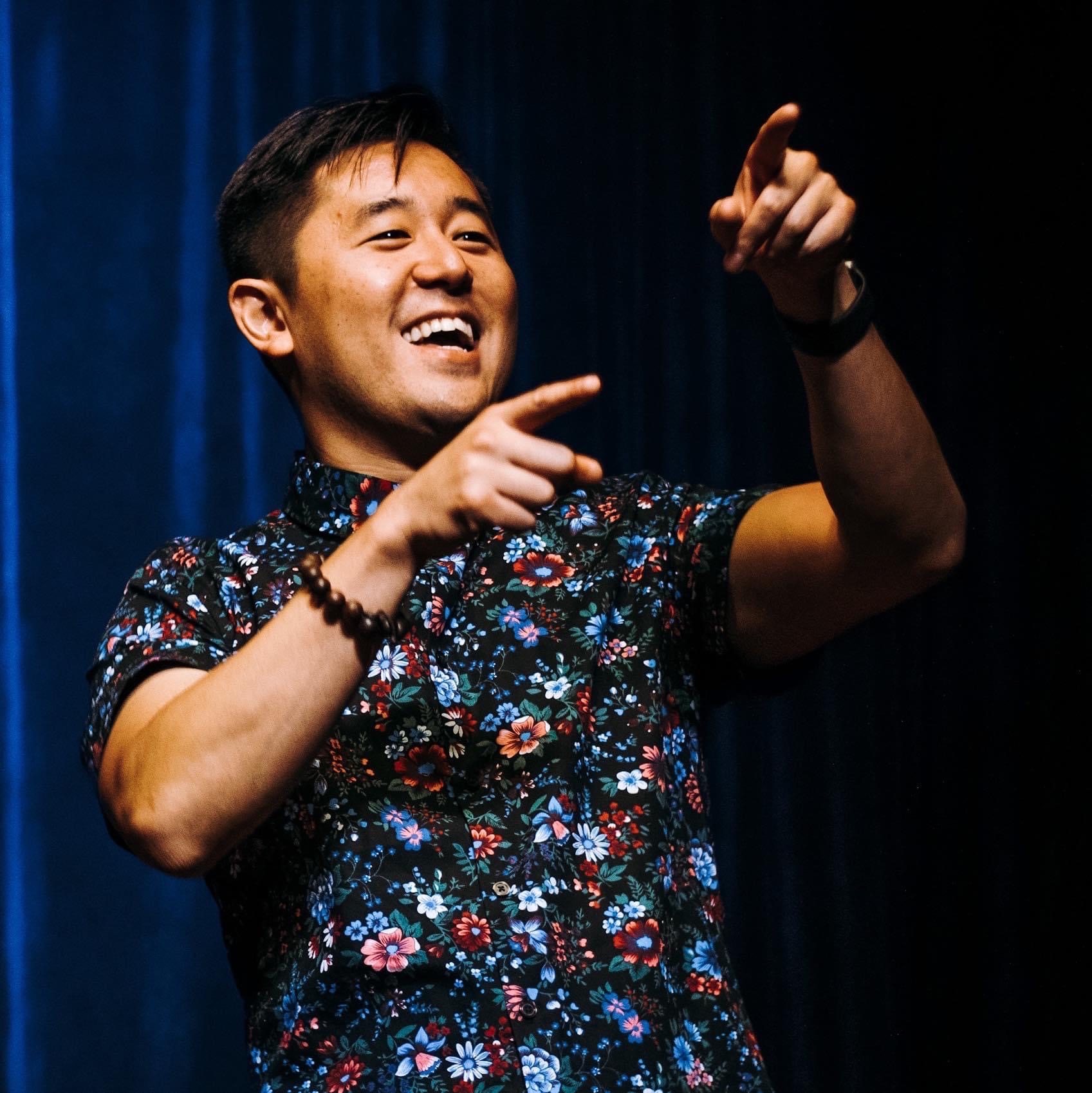 Man in blue print shirt with raised hand onstage