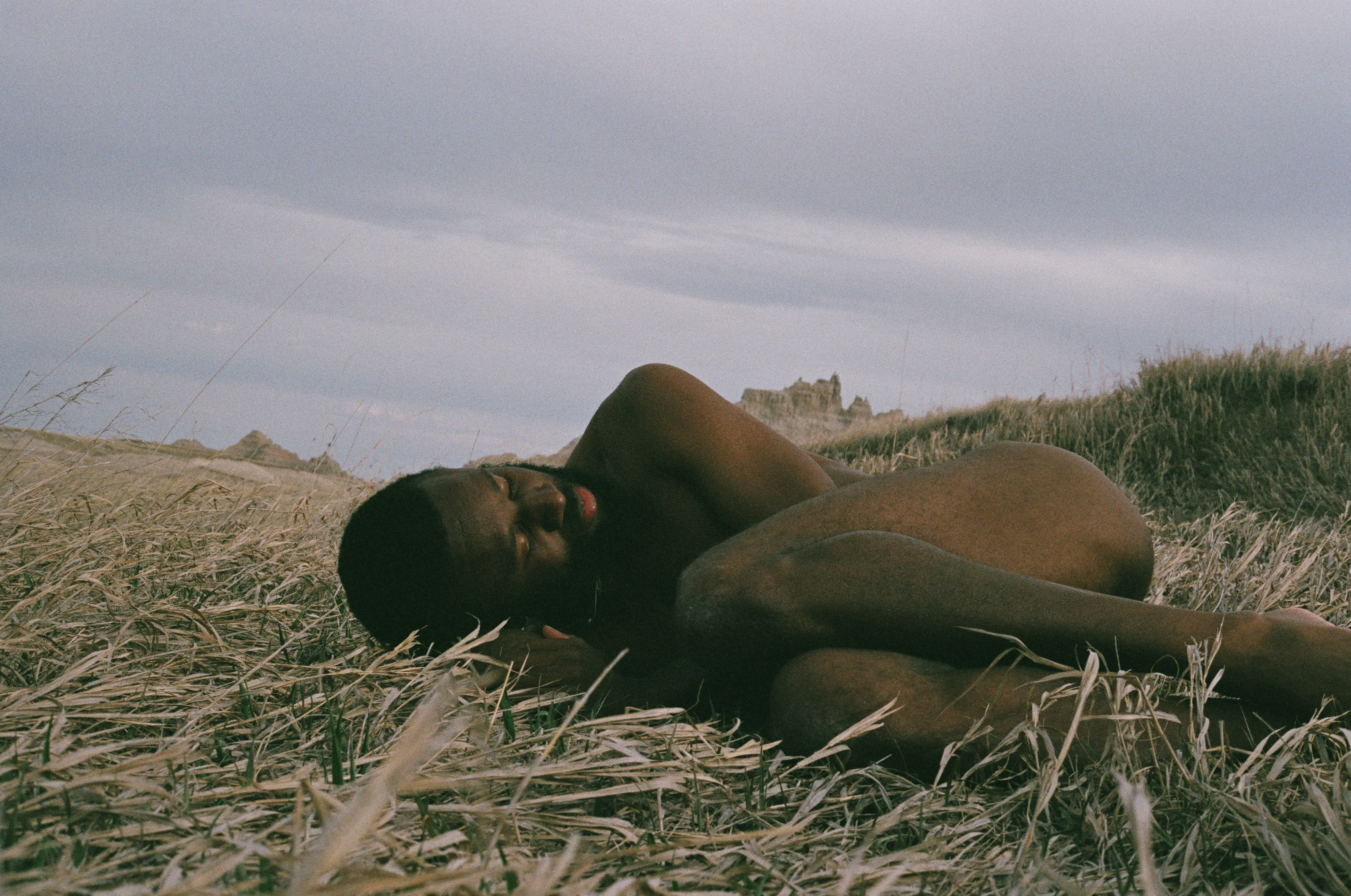 Unclothed man in fetal position in a field