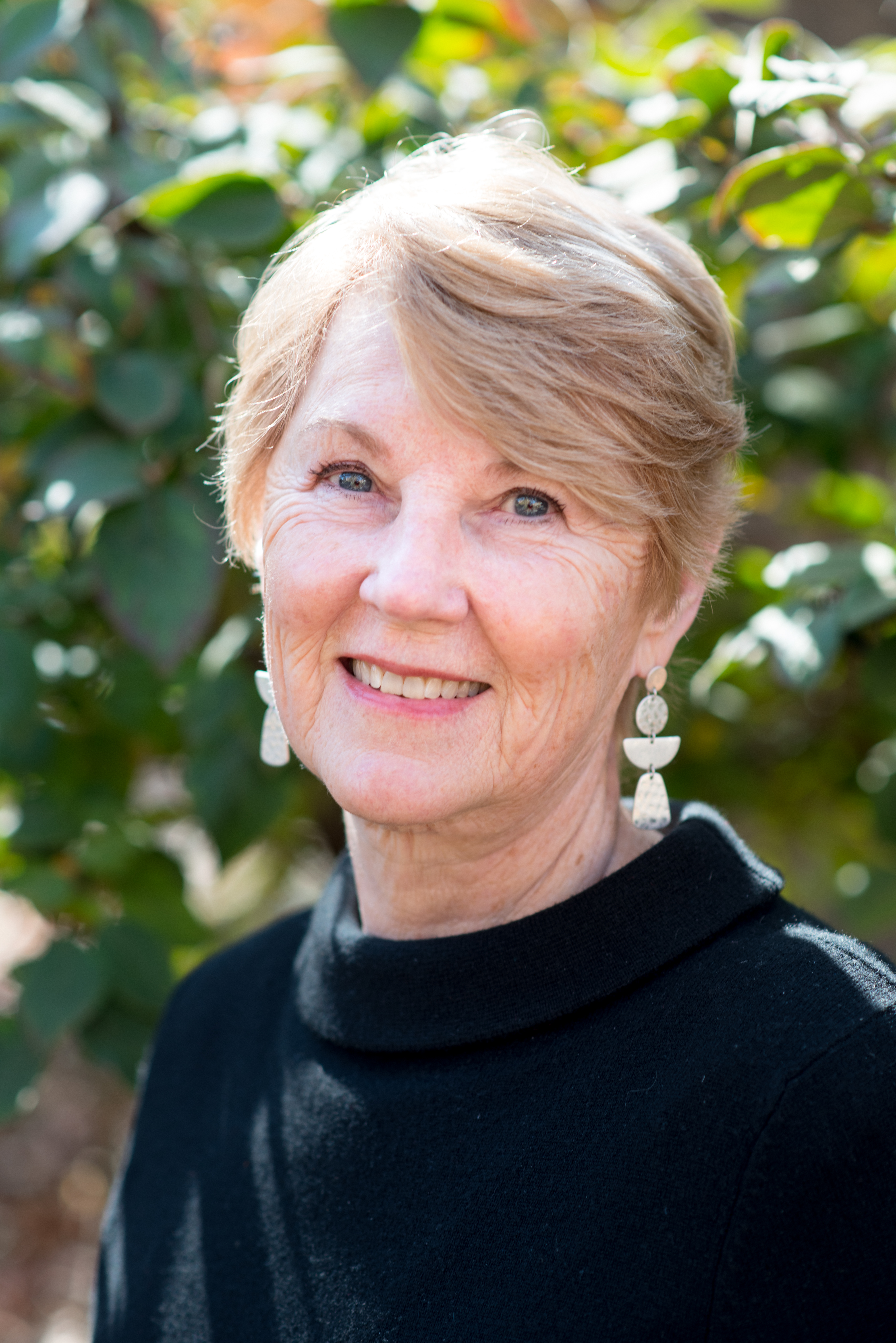 Boyer, dressed in black and looking over her left shoulder at the camera with greenery in background.